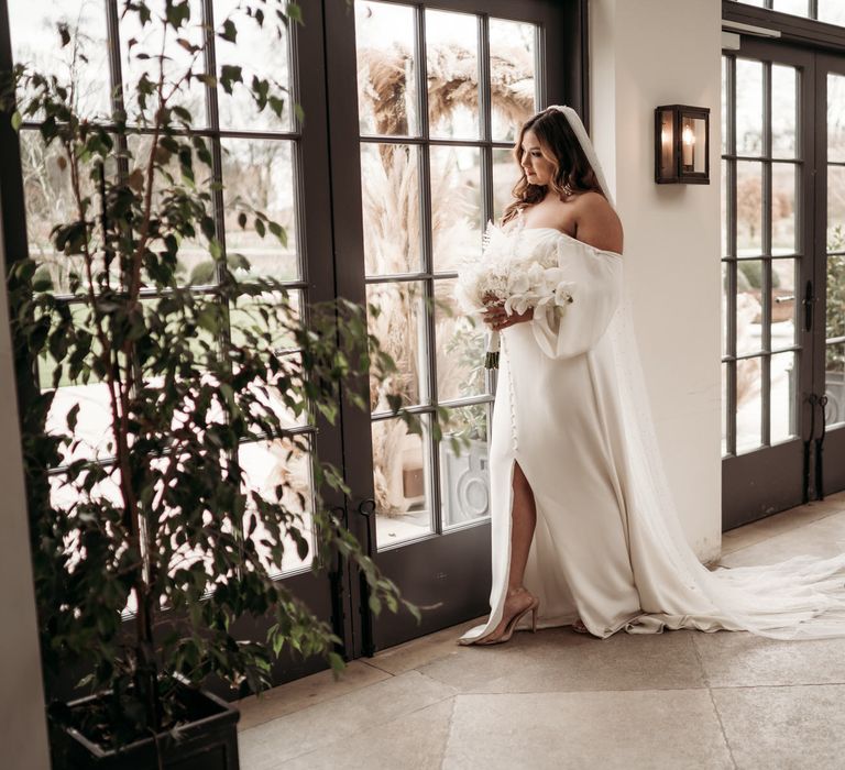 beautiful bride in a strapless wedding dress with front split and button detail holding an all white wedding bouquet 