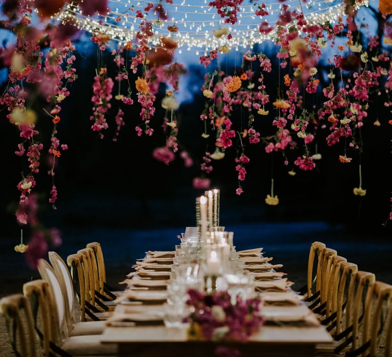 Suspended floral installation and fairy light canopy over rustic wooden wedding table at enchanted forest wedding in Italy