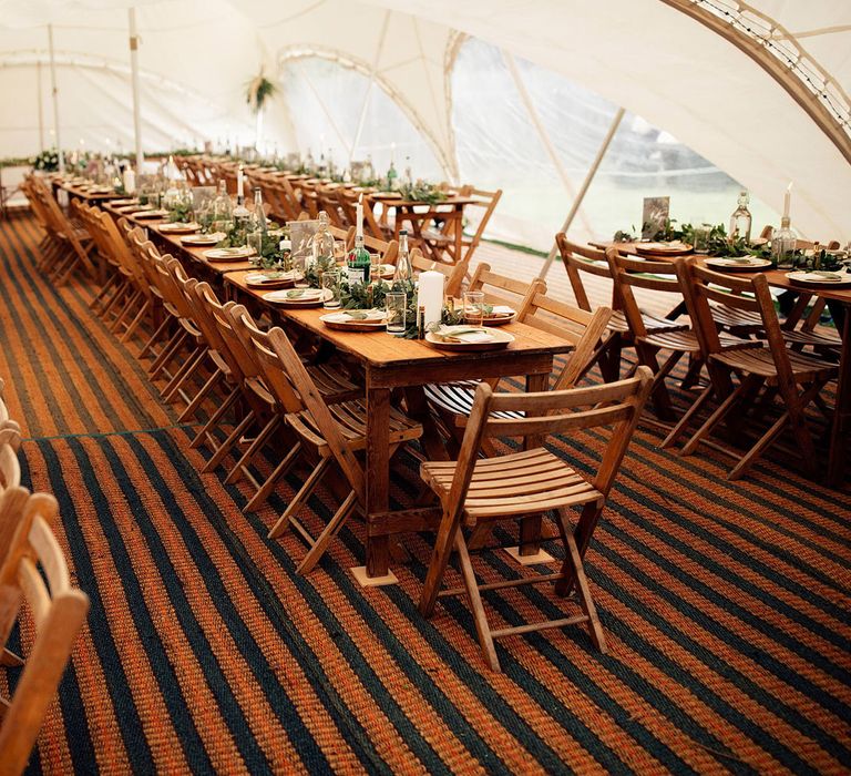 Interior of wedding marquee with brown and black striped carpet, wooden table and chairs and foliage table decor with candles