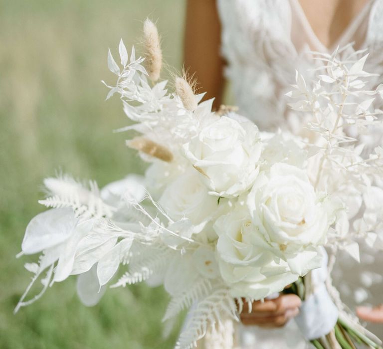 Bride holding all white bouquet including roses, pampas grass and white leaves