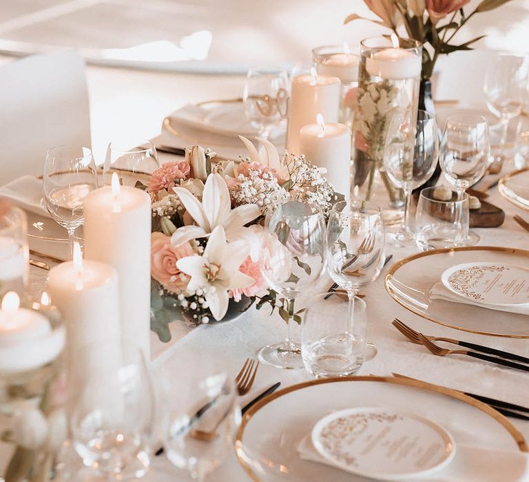 Tablesape with gold rimmed glass plates, black and gold cutlery and pink and white centrepiece flowers