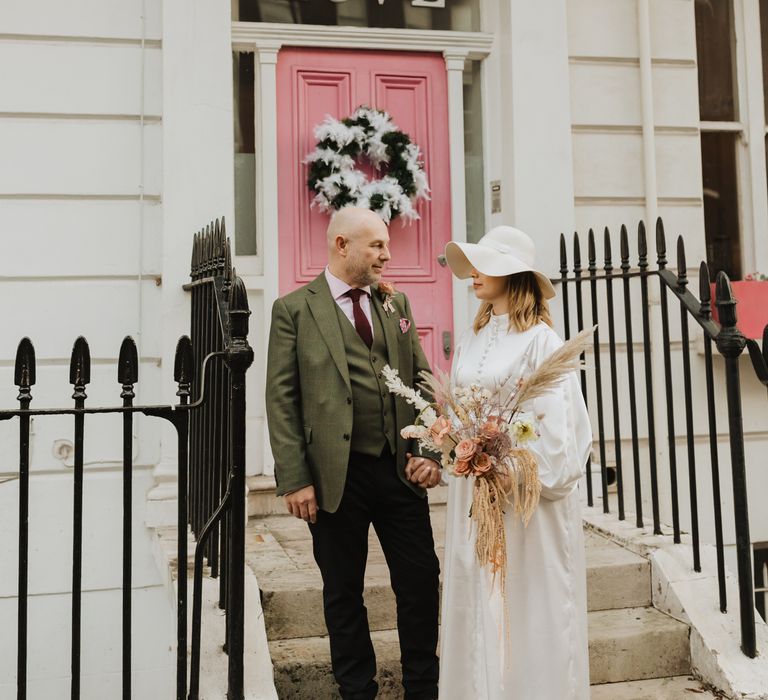 Bride & groom stand in front of pink door with one another on wedding day