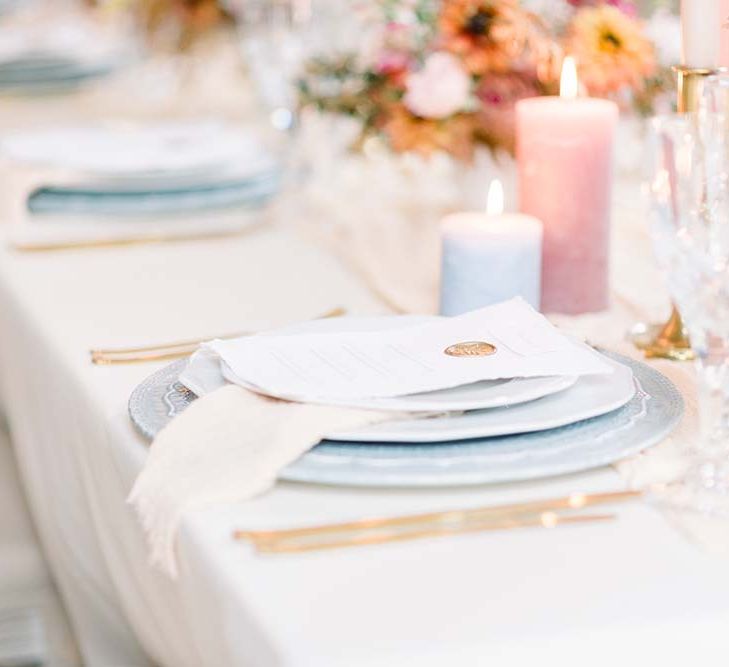 Elegant place setting with blue tableware, gold cutlery and wax seal menu card