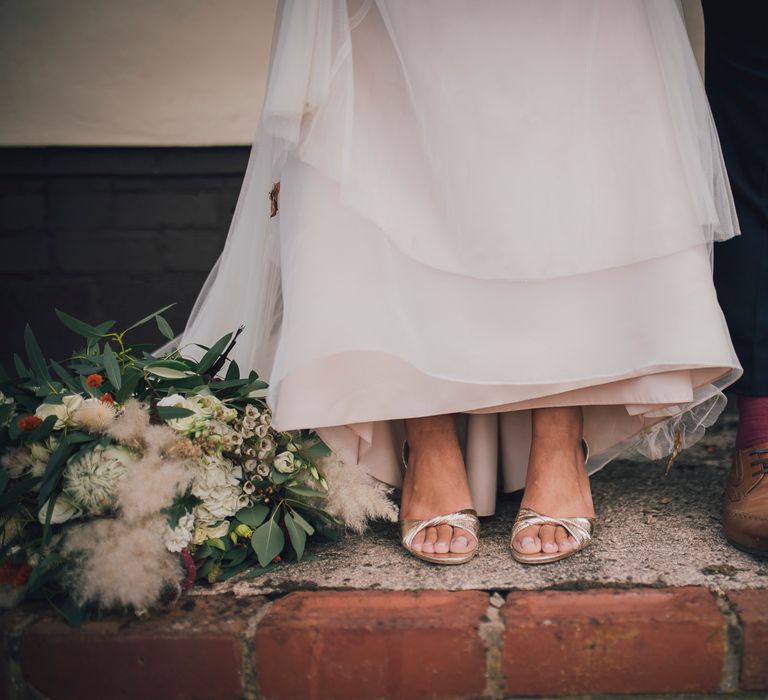 Bride wears gold sandal heels and groom wears brown brogues with burgundy socks