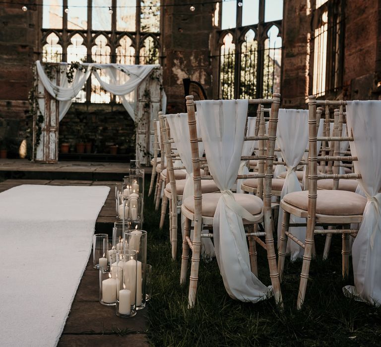 Outdoor wedding ceremony at St Lukes Bombed Out Church in Liverpool with chiffon chair back covers and pillar candles lining the aisle 