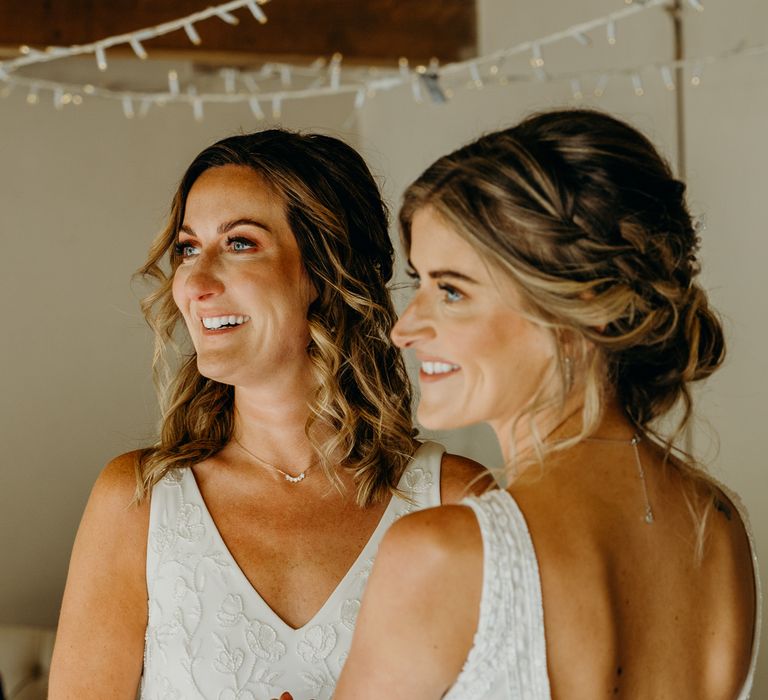 Brides wear hair in loose curls and braids whilst holding hands and looking toward celebrant during wedding ceremony