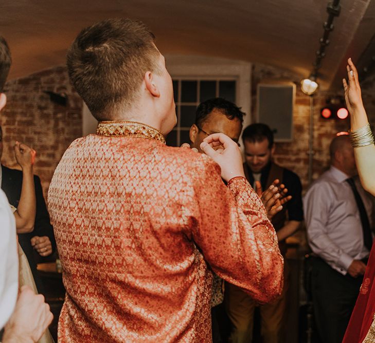 A bride in glasses and a traditional lehenga as she dances at her wedding party. 