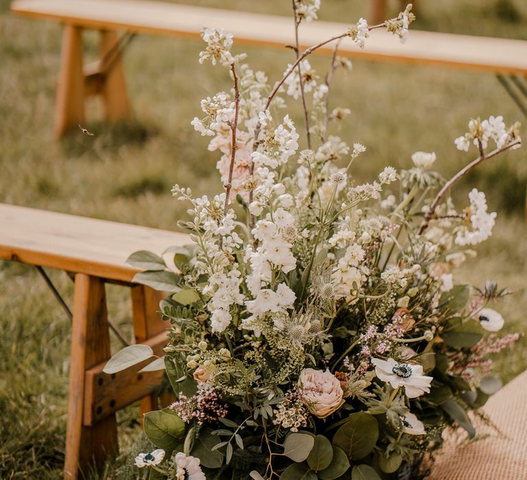 Mixed floral display with white, pink and green florals in white woven basket by wooden bench at Dunluce Castle wedding