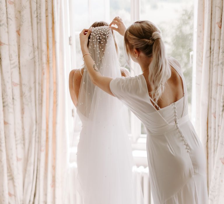 Bride has pearl veil applied to her hair on her wedding day