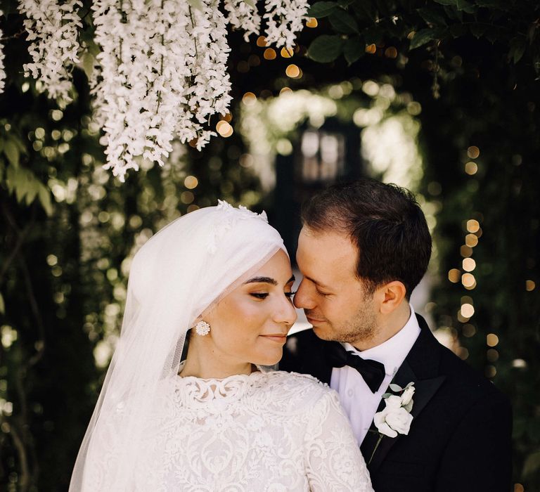 Pale pink roses and white orchid wedding bouquet held by bride with groom under hanging wisteria