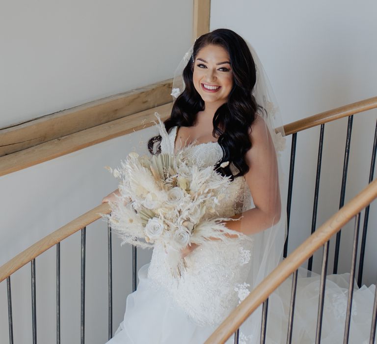 Beautiful bride in a strapless fishtail wedding dress walking down the stairs holding a dried flower wedding bouquet 