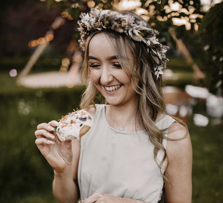 Bridesmaid in a grey satin wedding dress and dried flower crown eating a doughnut 