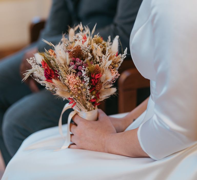 Bride holds vibrant small dried flower bouquet tied with white silk ribbon