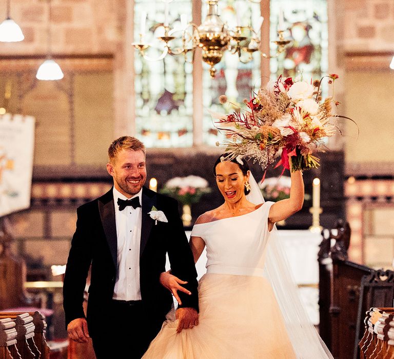 Bride lifts bouquet as she walks down the aisle with groom