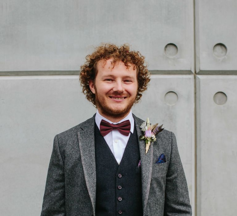 Groom with curly hair in a grey wool wedding suit with contrasting waistcoat and bow tie 