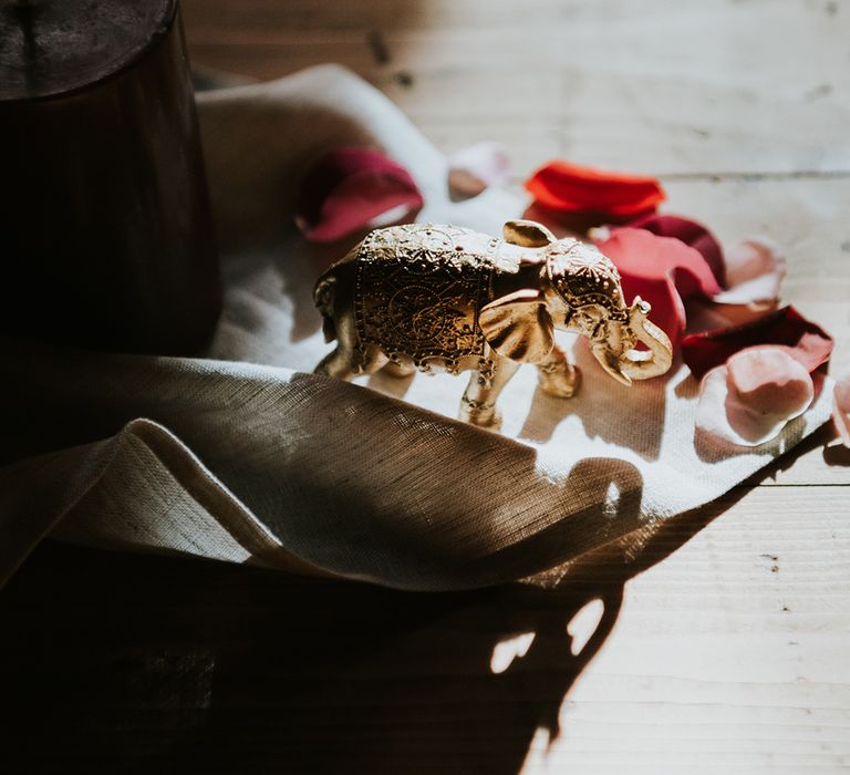 A small gold elephant statue stands on a table runner as decor at an Indian British wedding.