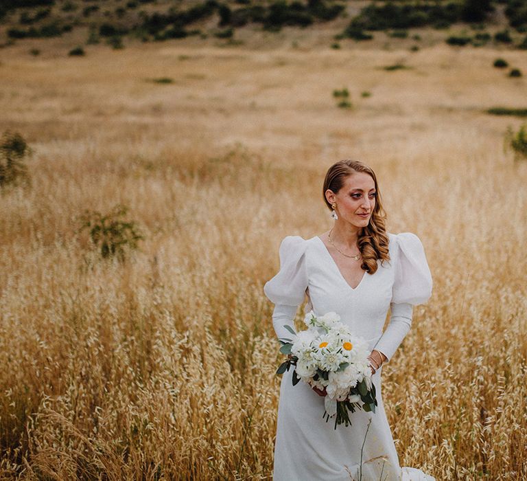 Bride holds white floral bouquet as she stands within golden fields