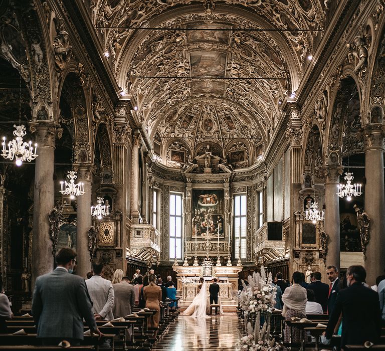 Bride and groom stand at the front of beautiful gilded church in Italy complete with pampas grass floral installations  