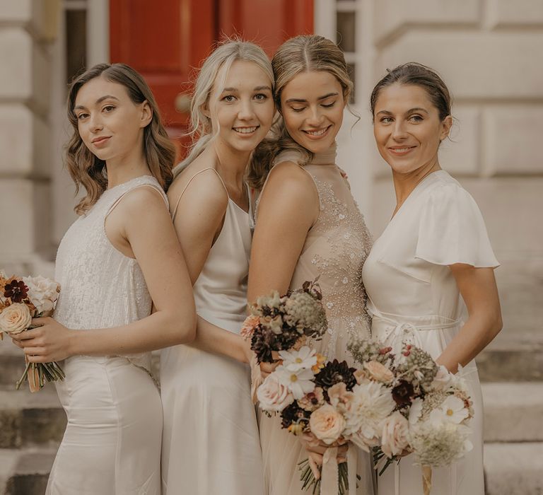 Bridal party portrait with bride in a tulle halterneck wedding dress and bridesmaids in white satin facing each other 