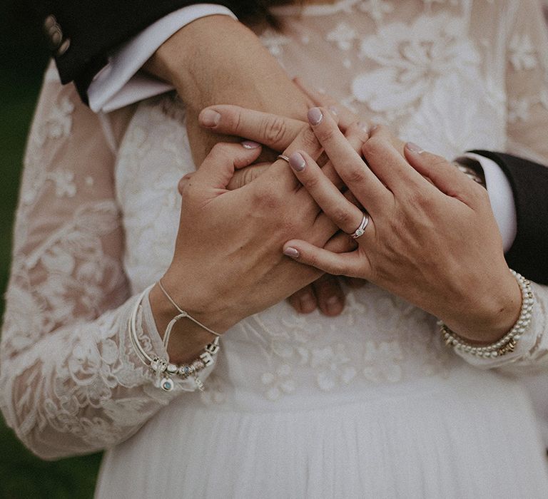 Groom embracing his bride with light pink wedding nails wearing her diamond engagement ring and wedding band 