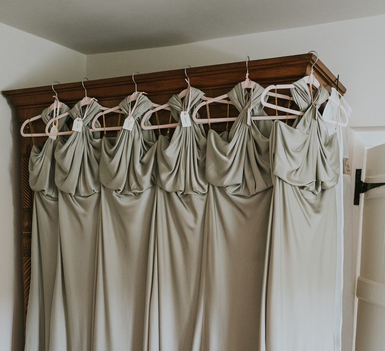 Six sage green satin bridesmaid dresses hanging on wooden wardrobe for summer wedding at Primrose Hill Farm