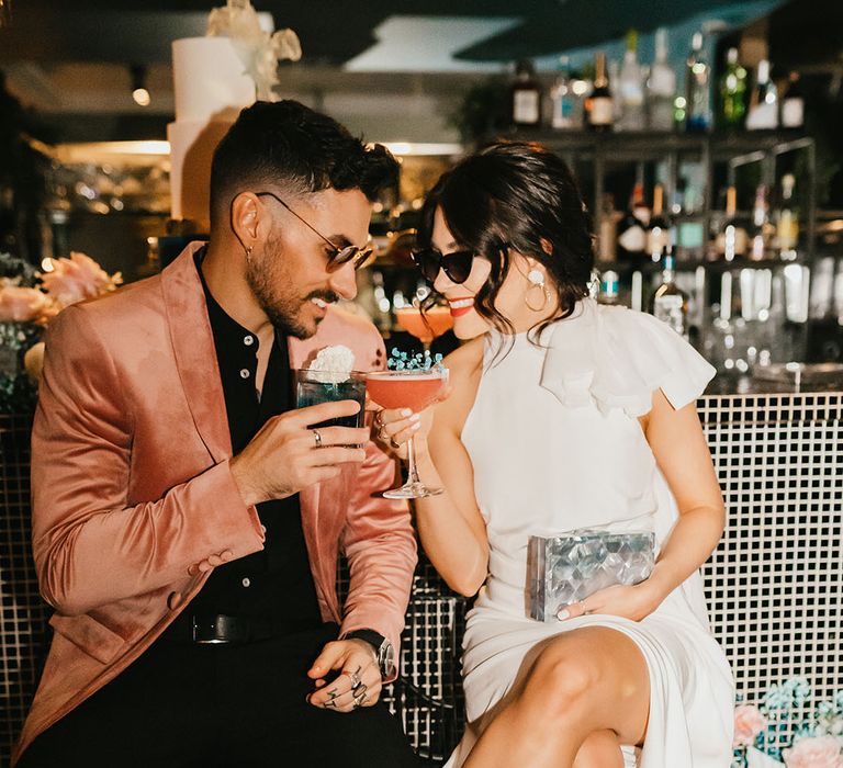 Stylish bride and groom sipping cocktails at the bar at their pink and teal city wedding 