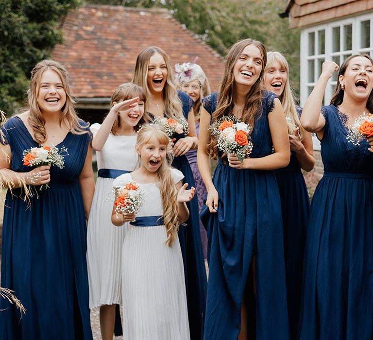 Bridesmaids smile as they see bride for the first time whilst holding floral bouquets and wearing royal blue dresses from Depop