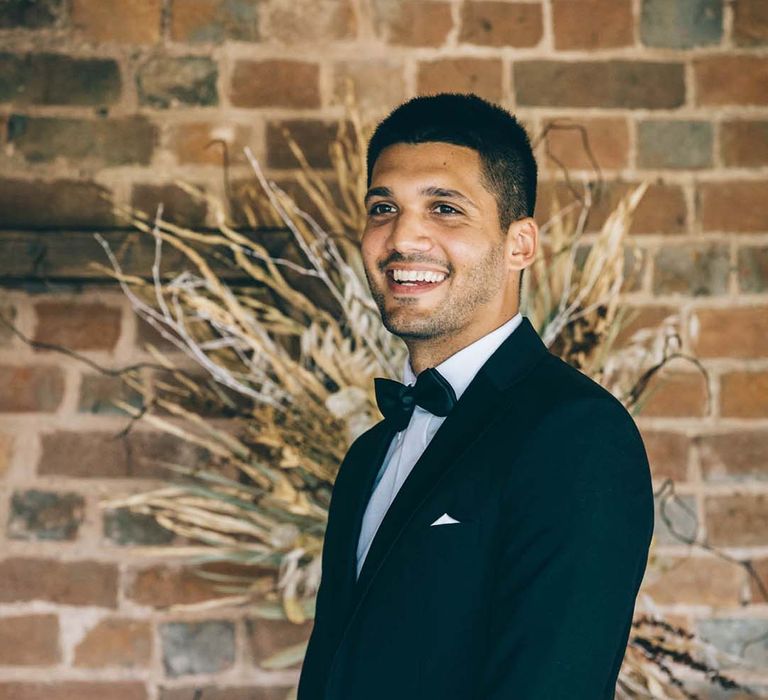 Stylish groom in a tuxedo and bow tie standing at the altar at Brickhouse Vineyard 