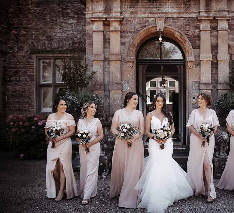 Bride in Eeysee Bridal wedding dress that fits perfectly stands with bridesmaids in nude silk long dresses with bouquets of delicate flowers 