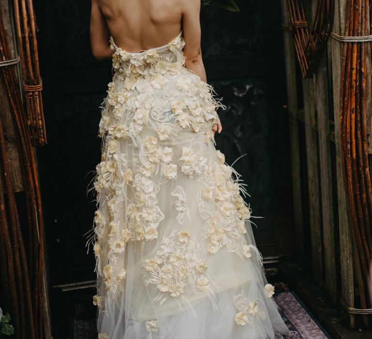 Bride in strapless feathered appliqué wedding dress stands in doorway at rustic wedding in Lancashire