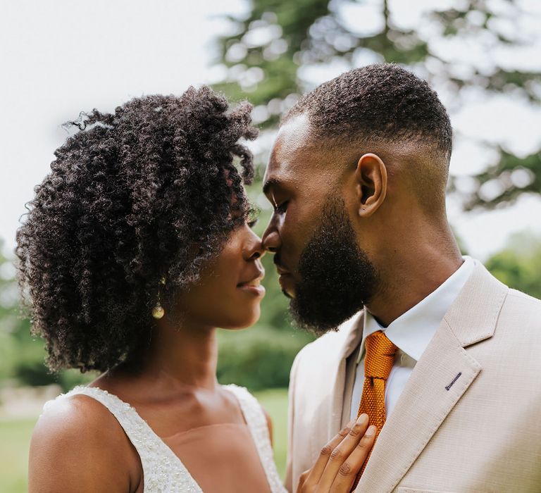 Black bride in an embellished plunging neckline wedding dress embracing her groom in a beige suit 