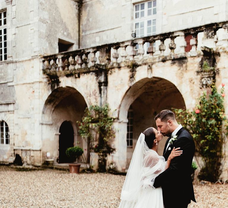 Bride & groom kiss in front of French Chateau wedding venue