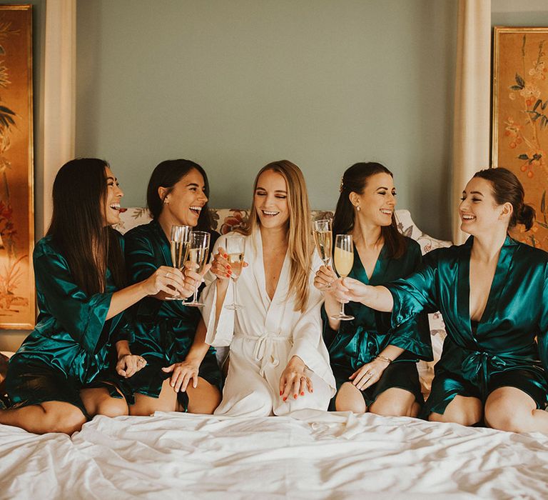 Bride sits with her bridesmaids who wear green satin dressing gowns 