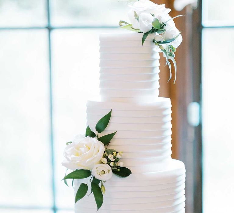 Elegant white wedding cake with white roses and foliage decor 