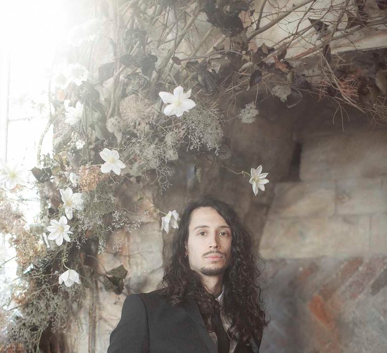 Stylish groom with long wavy hair and a beard wearing a dark wedding suit 