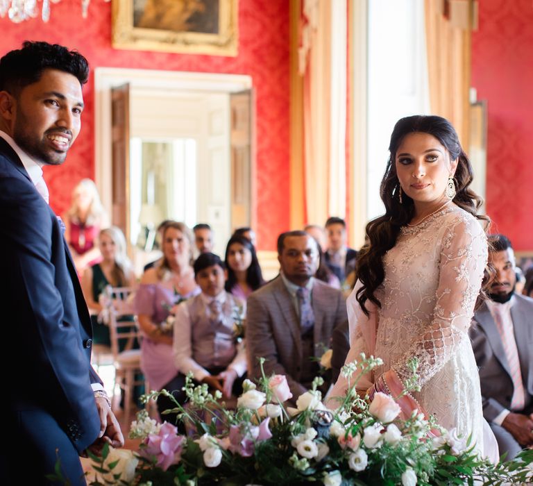 Bride & groom look toward celebrant during ceremony as wedding guests watch on