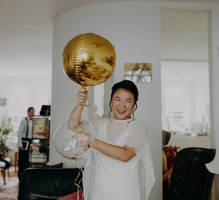 Bride holds gold balloon as she wears wedding dress sample complete with cape  | Irene Yap Photography