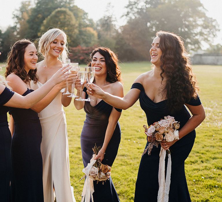 Bride and bridesmaids in navy blue bridesmaid dresses share a toast together at country house wedding