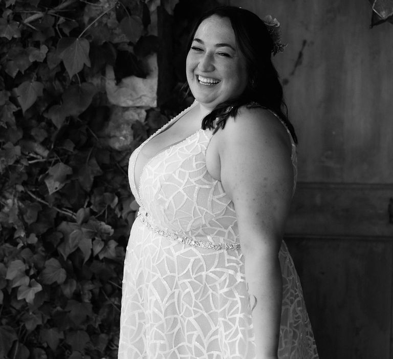 Smiling bride with brown half up half down hairstyle with flowers wears v-neck geometric patterned wedding dress