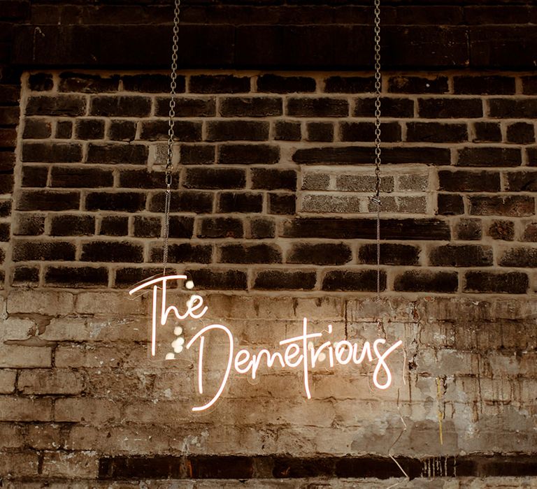 Custom pink neon sign with couple's last name saying, 'The Demetrious' on exposed brick wall 