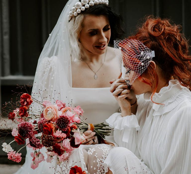 Bride in a high neck wedding dress with long sleeves and perl encrusted bidcage veil kissing her brides hand in a pearl headband 