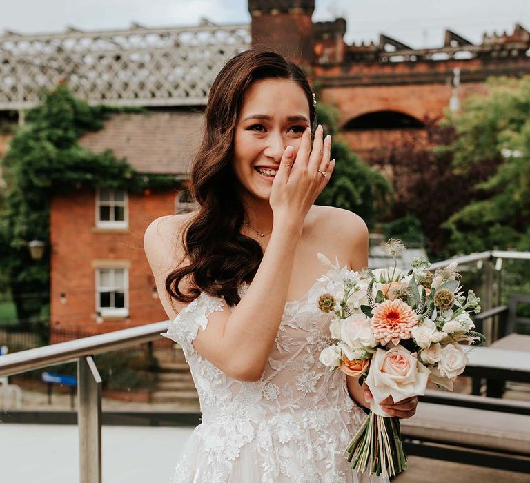 Bride in flower lace and tulle gown wipes her eyes after seeing her groom for the first time on terrace in city centre