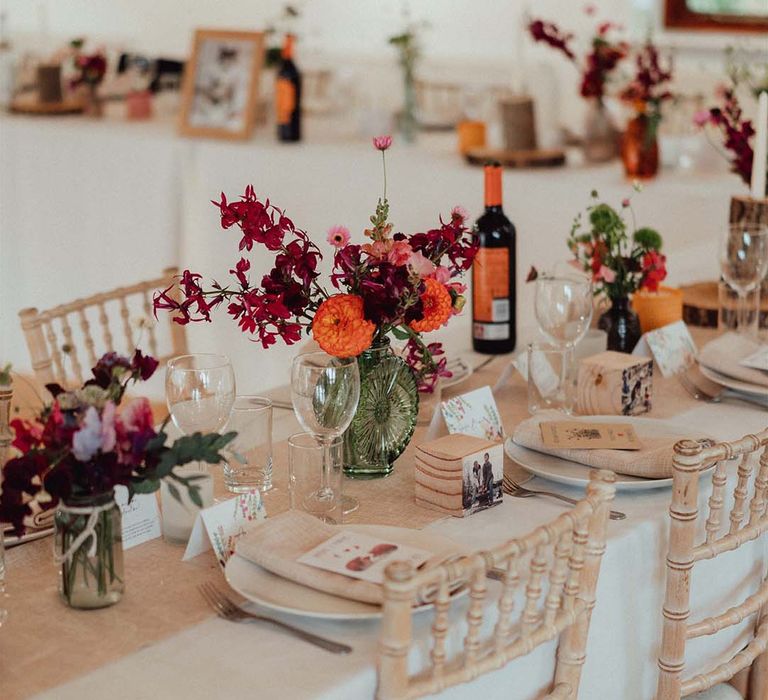 Colourful pink, red and orange wedding flower arrangements in green glass vases for wedding table settings 