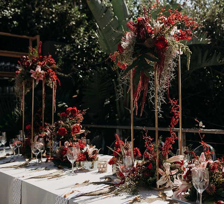 Bright and bold red and pink wedding flower arrangements and tall centrepieces for outdoor table settings