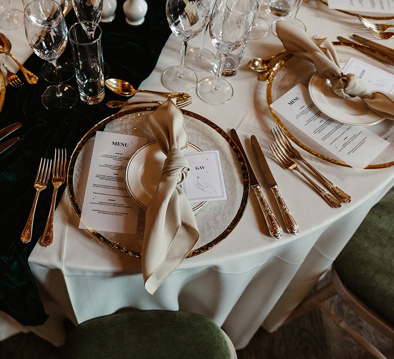 Table setting with white card with hand and stars on for name place card, green table runner and gold cutlery and plate with black candles