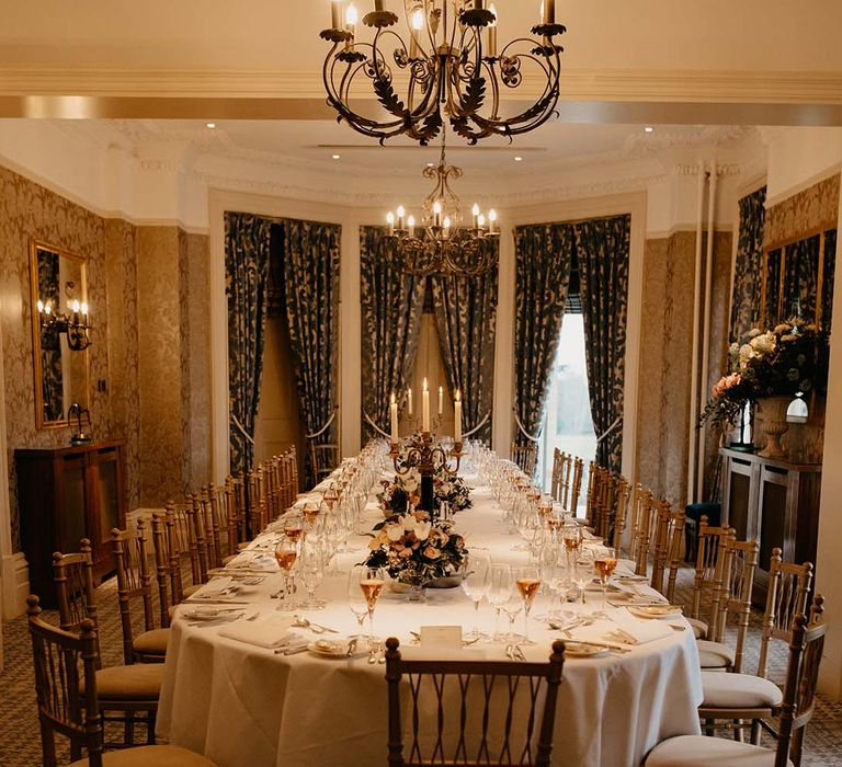 Large wedding tablescape with neutral mixed floral displays, wine glasses full and large draping green and gold curtains