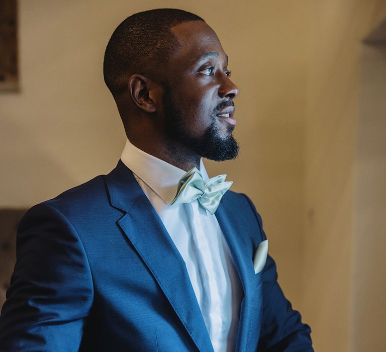 Dashing groom in blue suit with mint green bow tie and handkerchief