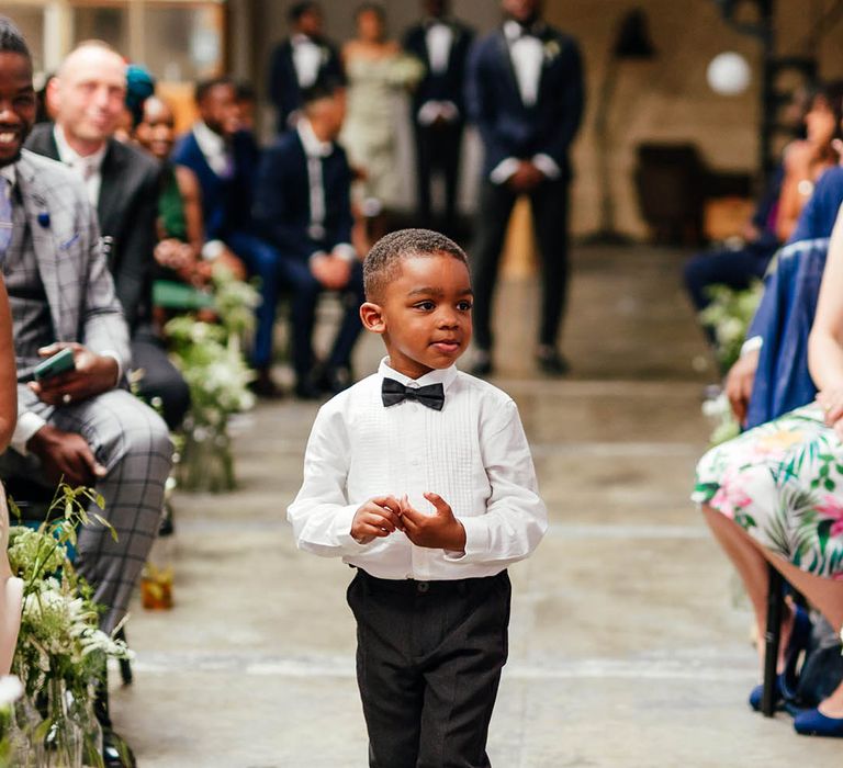 Young page boy in black tie and white converses walks up the aisle