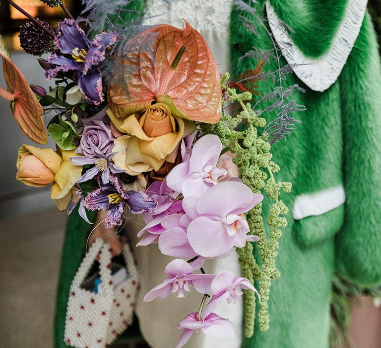 Pink, orange, yellow and purple wedding bouquet with roses and orchids next to bridal green fur jacket cover up