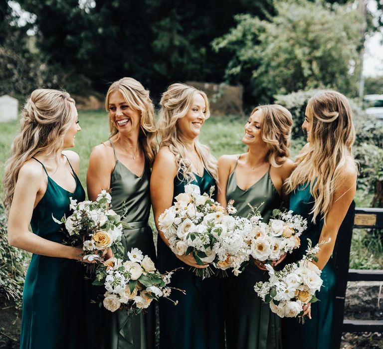 Bridesmaids in different shades of green satin dresses with neutral bouquets